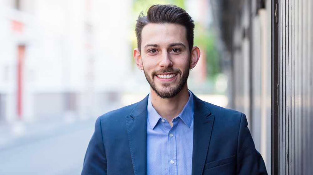 relaxed professional headshot, bearded young man in dark blue suit in outdoor setting