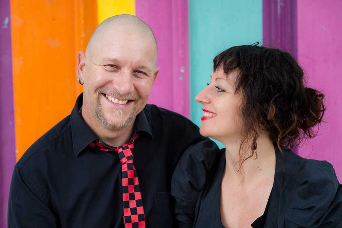 couple dressed in balck against brightly coloured wall, girl looking at guy