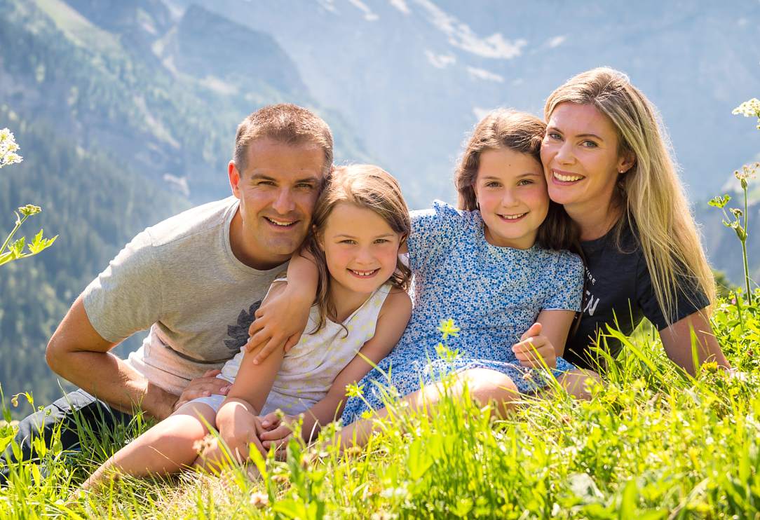 Family of four sitting cuddled up in alpine meadow high in the mountains