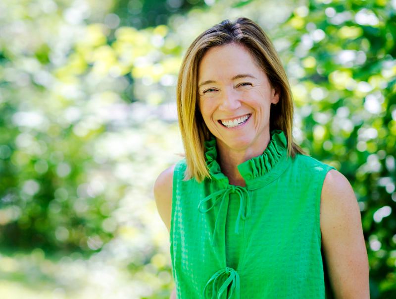 smiling young female business owner in bright green top against sunlit leafy background